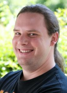 Headshot of Timothy Brick with long brown hair and black shirt.